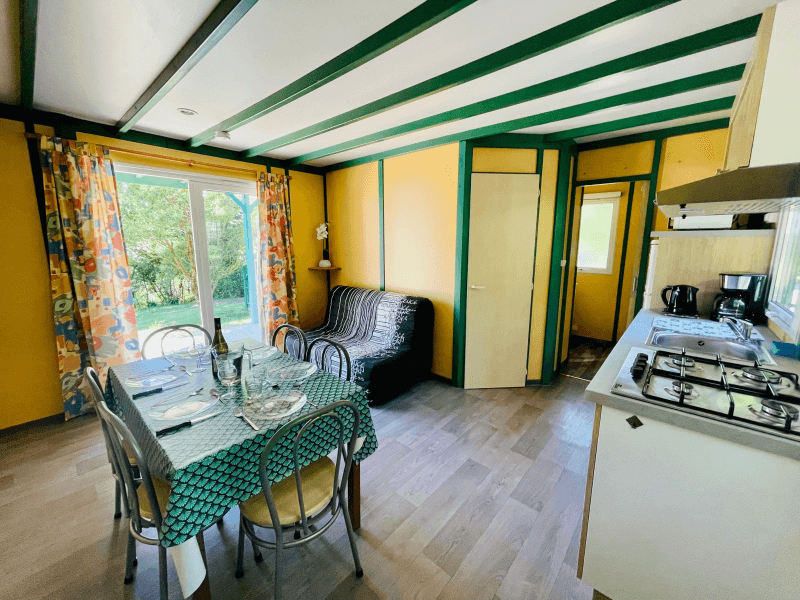 Salon avec canapé et coin cuisine. Location Chalets en Ariège, chalets Epicéa conforts 6 personnes