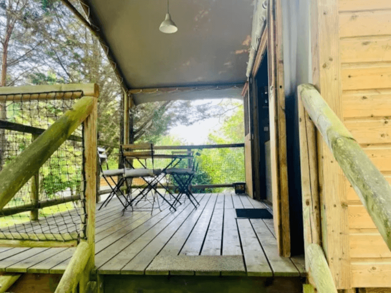 Grande terrasse en bois couverte avec salon de jardin en bois, du Lodge Èrable Confort. Le glamping à Camon en Occitanie