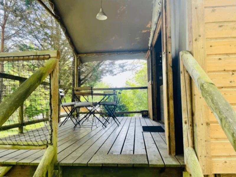 Large covered wooden terrace with wooden garden furniture, at Erable Lodge Comfort. Glamping in Camon, Occitanie