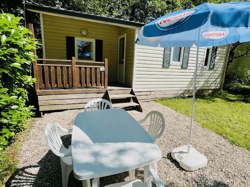 Covered wooden terrace with garden furniture and parasol. Mobile home rental in Camon in Occitanie, comfort Frêne mobile home 4 people