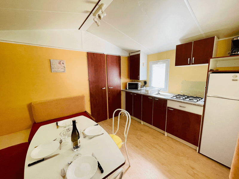 Kitchen/living area with bench and table. Mobile home rental in Ariège, comfort Frêne mobile home 4 people